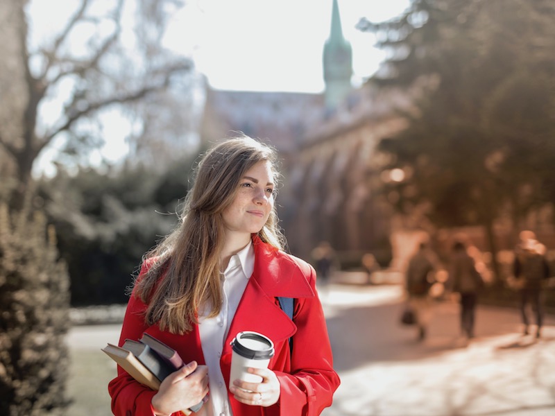 Woman walking around on campus with books and coffee in her hands.