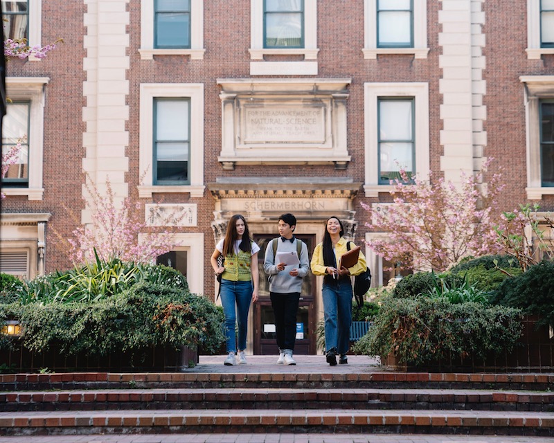 Three college students walking on campus down the steps of their university.