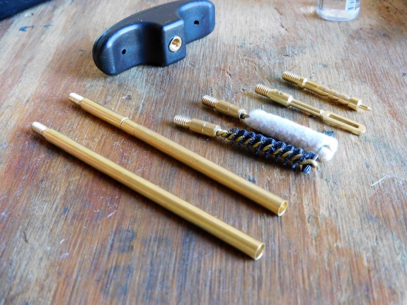 A brass cleaning rod laid next to brushes and jags, from gun cleaning kit