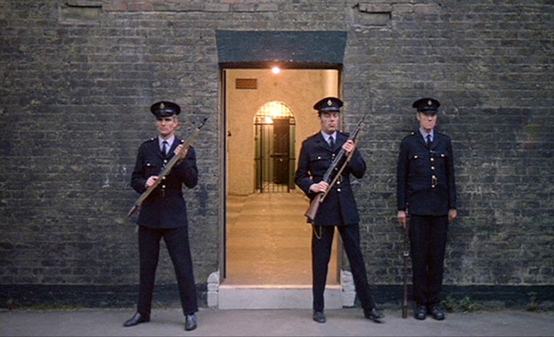 three armed guards stand outside an open door