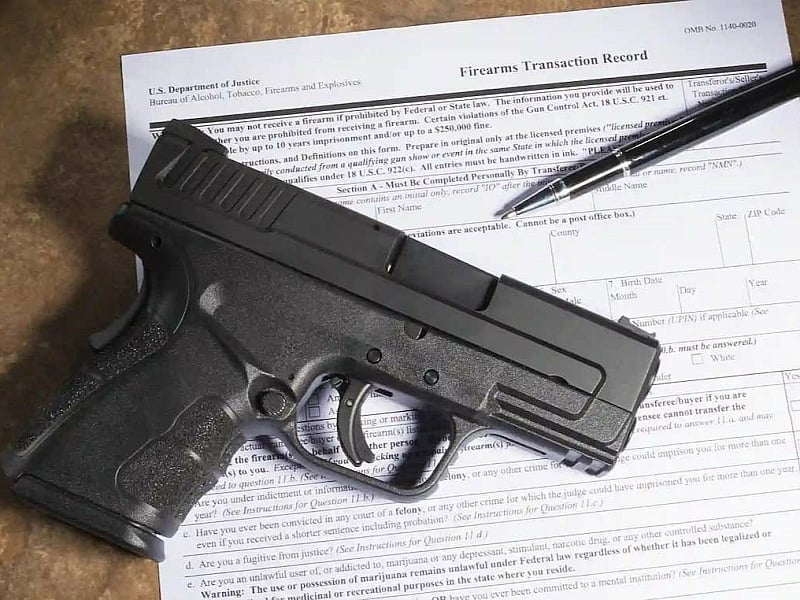 A pistol and pen on a Federal firearms background check form